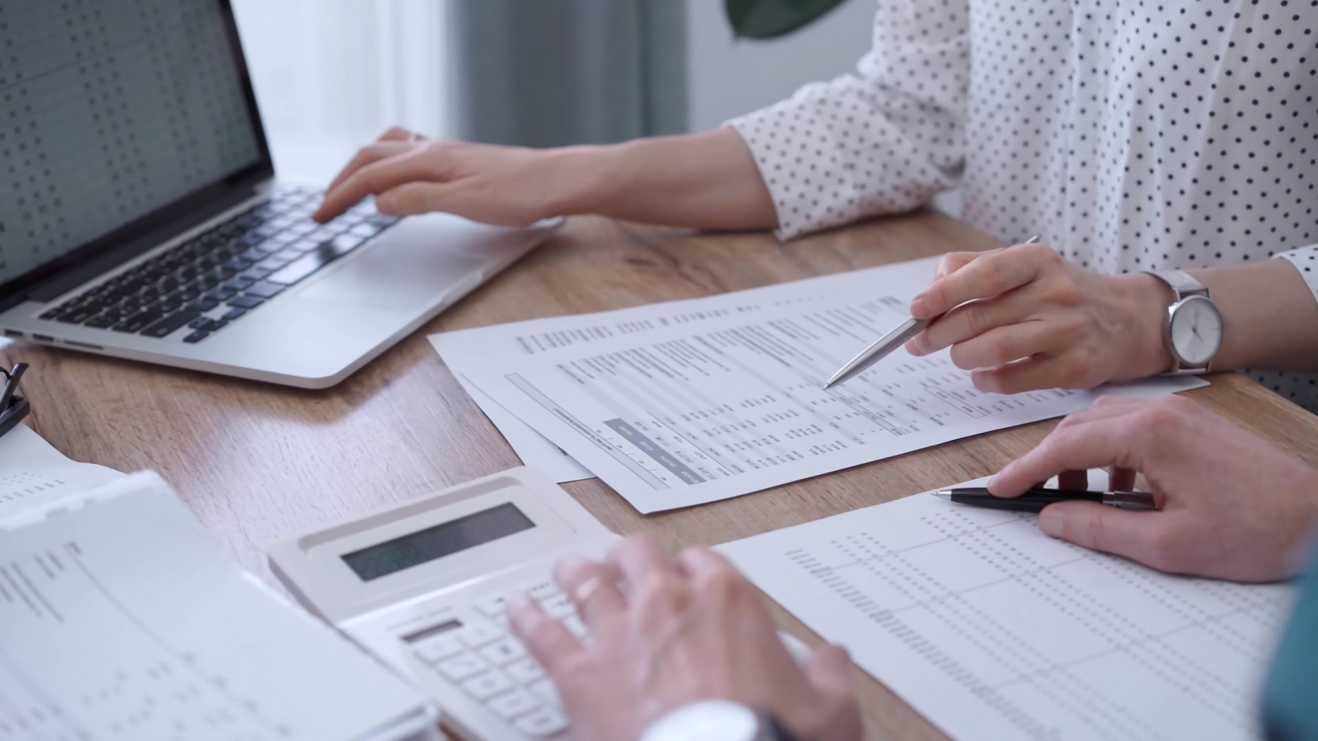 Two bookkeepers reviewing financial statements and using a calculator at a desk